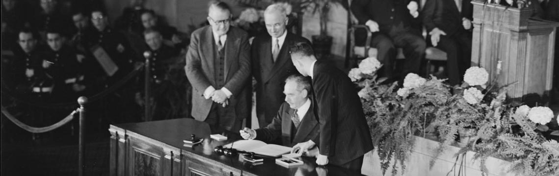 Photo of Secretary of State Dean Acheson signing the Treaty and President Truman looking over his shoulder